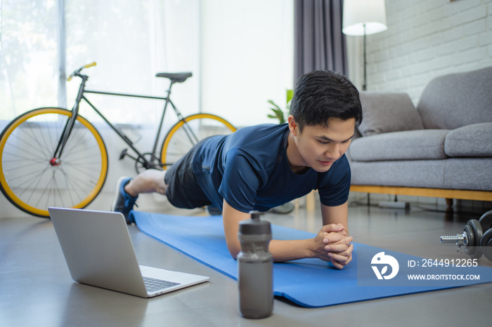 Sporty man doing yoga plank while watching online tutorial on laptop, He exercising in living room.