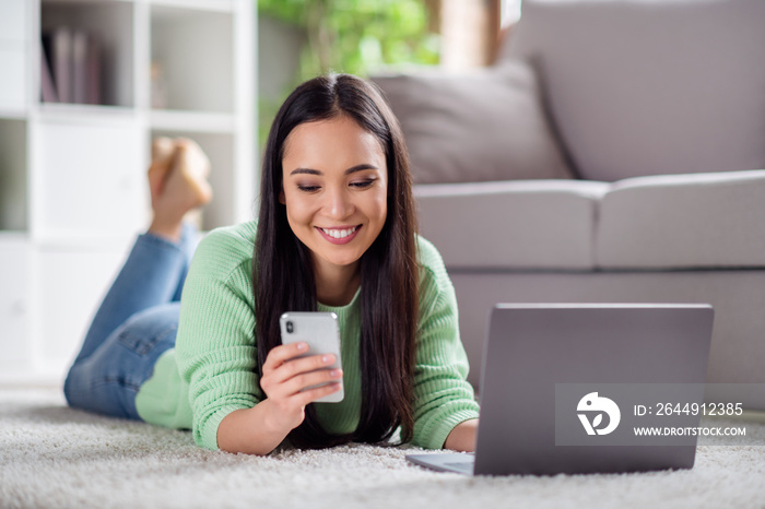 Close up photo of positive chinese girl work laptop use smartphone check social network notification lie floor carpet in house indoors