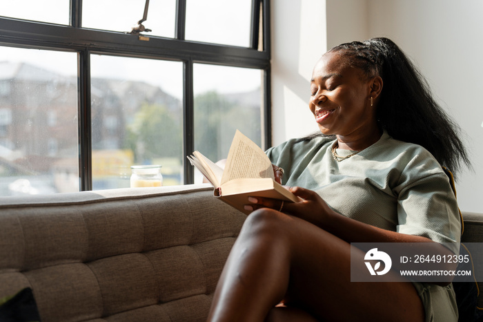 Young woman reading book while resting at home