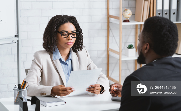 Focused female HR manager studying vacancy applicant’s CV during employment interview at office