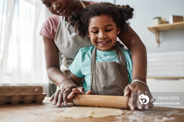 Loving mother and daughter baking together at home and rolling dough