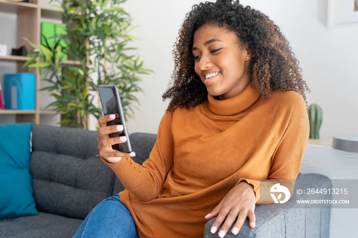 Young afro woman browsing on cellphone at home