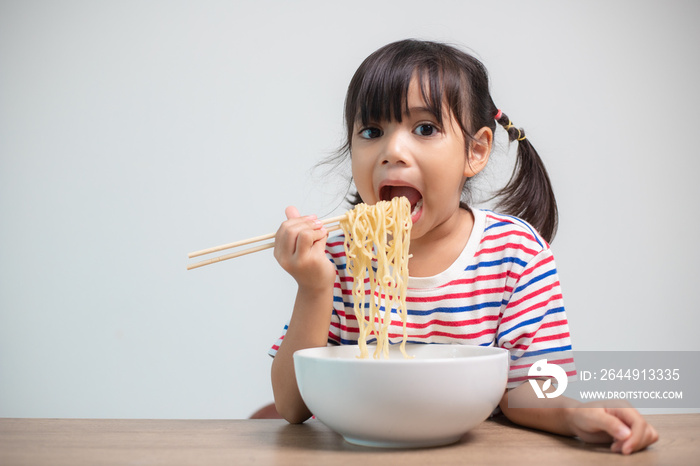 Cute Asian child girl eating delicious instant noodles at home.