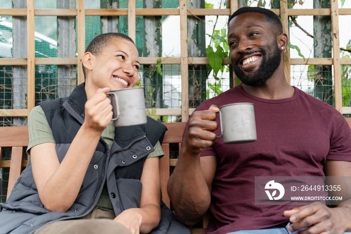 Smiling couple with metal mugs relaxing in urban garden