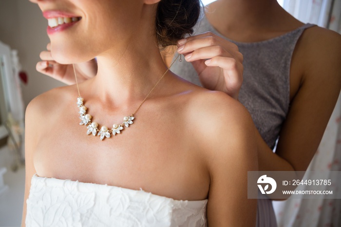 Midsection of bridesmaid fastening bride necklace in room