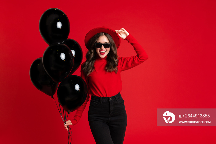 White woman in hat laughing while posing with black balloons