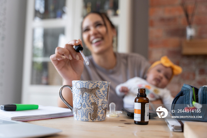 Mother adding vitamins to mug while holding baby girl at home