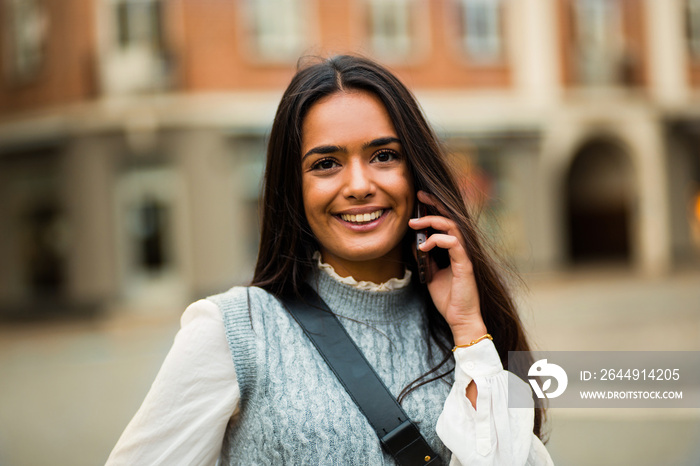 Woman standing on street and using mobile. Focus is on woman.  Talking on the phone.