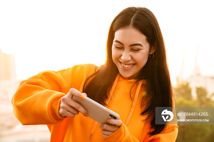 Photo of excited pretty asian woman playing video game on cellphone