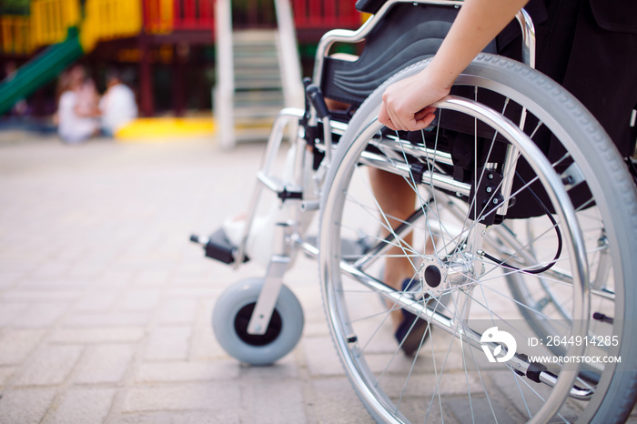 A girl with a broken leg sits in a wheelchair in front of the playground.