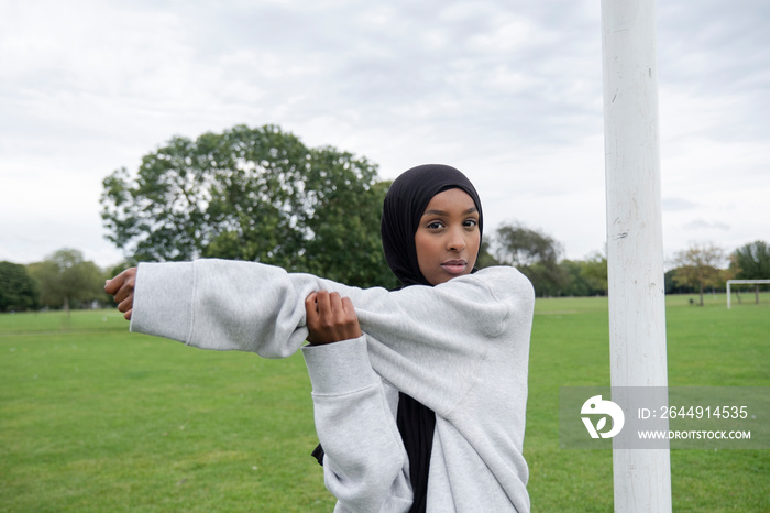 Portrait of woman in hijab stretching arm in soccer field