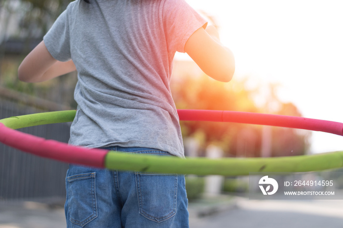 Adorable Asian child girl playing hula hoop in park for exercise in evening. Healthy Asia kid practice  hulahoop racing with light effect.