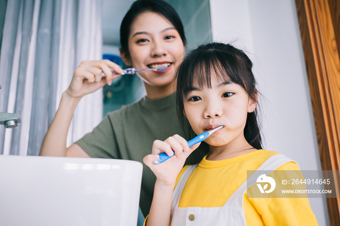 Mother and daughter brush their teeth together.