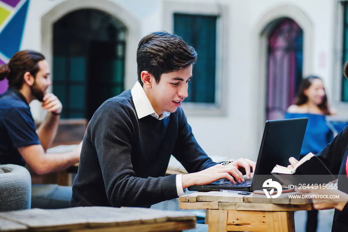 Young latin college man sitting while using computer at university in Mexico