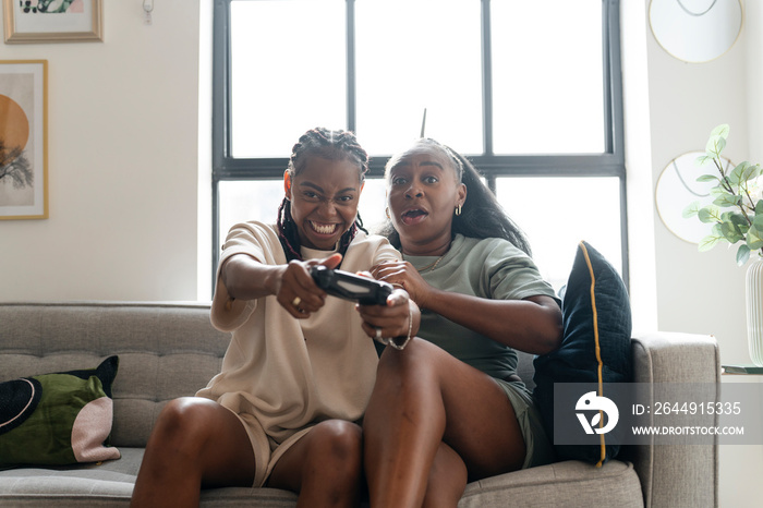 Lesbian couple playing video games while sitting on sofa at home