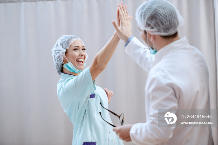 Smiling Caucasian doctor giving high five after successful surgery.