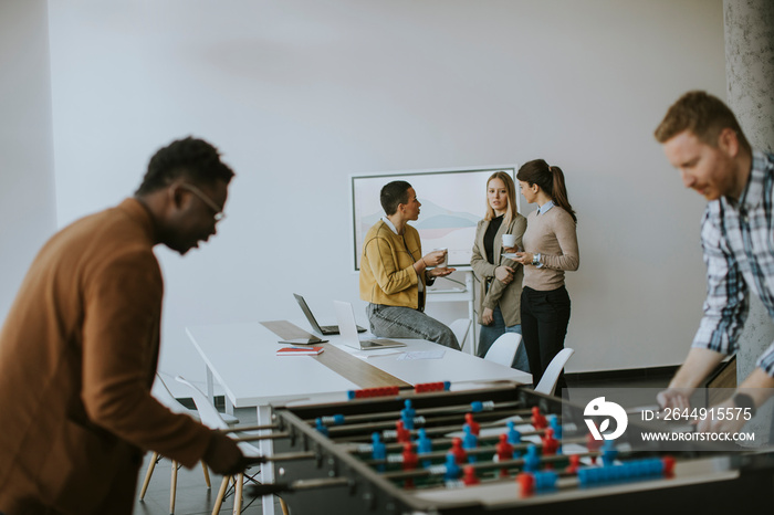 Young casual multiethnic business people playing table football and relaxing at office