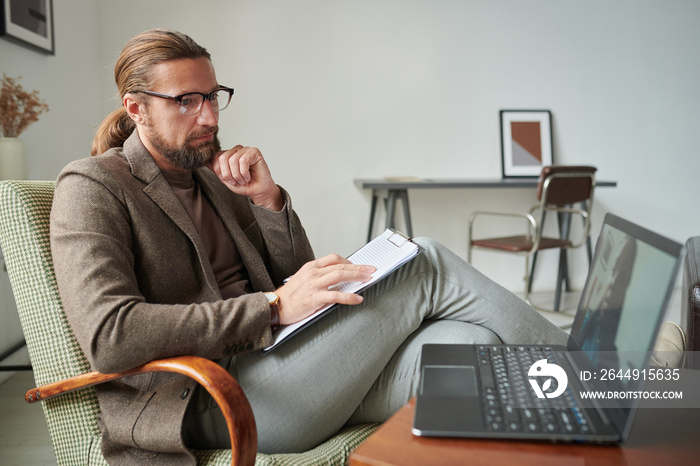 Serious psychologist talking to patient during online meeting, he sitting on armchair and listening to her problems