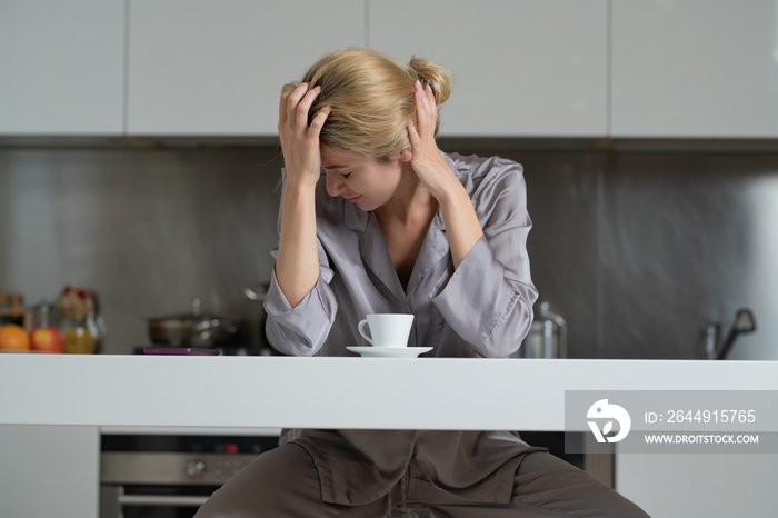 Depressed woman in the kitchen in the morning. Upset woman sitting in the kitchen watching phone in the morning and chatting smartphone. Sad tired housewife.