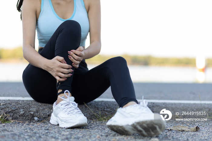 The female athlete suffered an ankle injury. A female runner has pain in her ankle. A runner sits down with a knee injury. The female athlete fell and had a bruise on her knee.