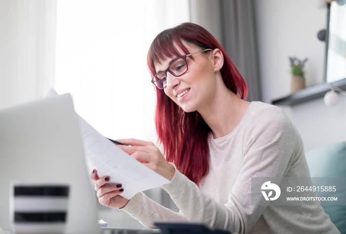 Happy woman at home using laptop and checking bills and invoice document