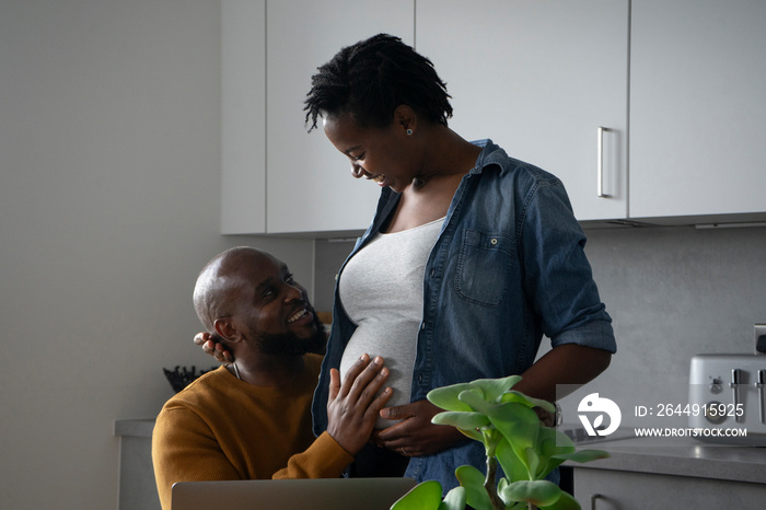 Smiling man touching pregnant woman’s belly in kitchen