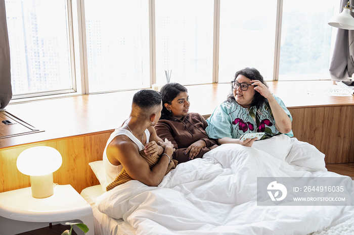 Three friends chatting and laughing together at home in bed