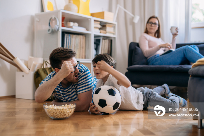 family watch soccer game at home together in living room. father and son cheers for their favorite team