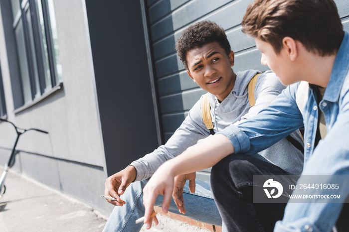 handsome and brunette boys sitting, talking and smoking cigarettes