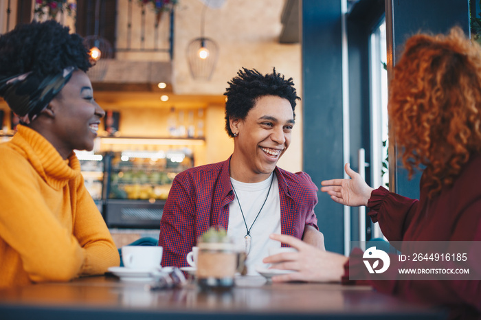 Three friends, two females and a male, sitting in a cafe, talking and having fun.