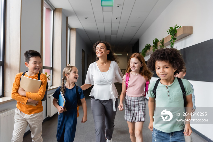 cheerful multicultural kids walking in school corridor with african american teacher