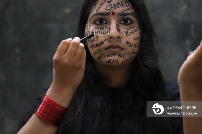 A southeast Asian brown young woman protesting gender based violence by writing anti violence against women and girls messages all over her face