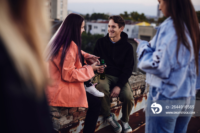 Three teenage friends sitting on the rooftop, chilling and drinking beer.