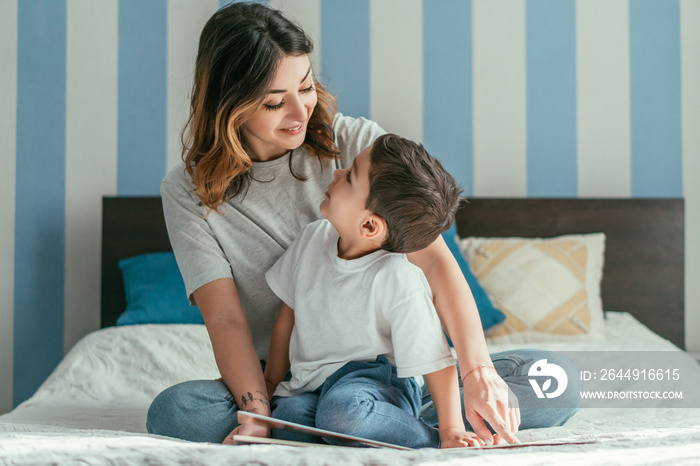 happy mother and cute toddler son looking at each other in bedroom