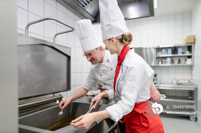 Chefs in large commercial kitchen cooking meals together stirring the sauce