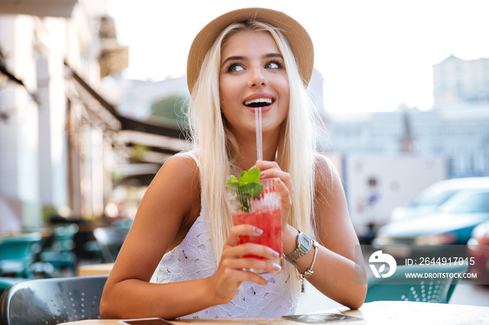 Beautiful young happy woman drinking cocktail while sitting in cafe