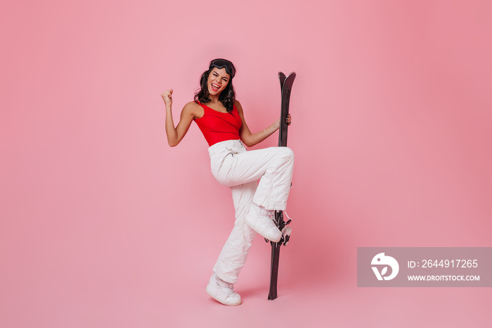 Blithesome woman in goggles dancing with smile. Sporty girl expressing happiness on pink background.