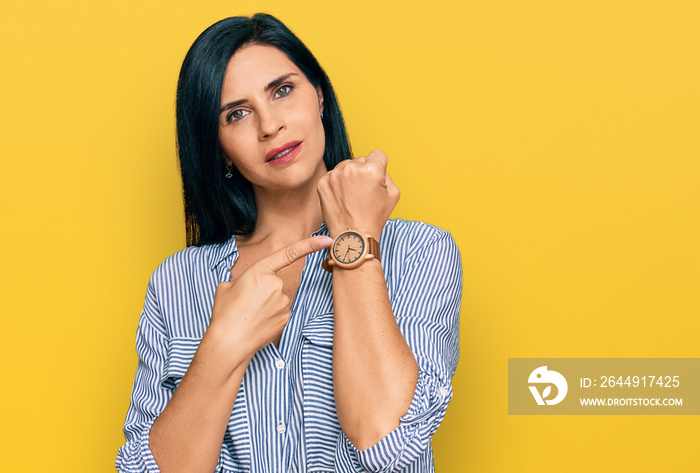 Young caucasian woman wearing casual clothes in hurry pointing to watch time, impatience, looking at the camera with relaxed expression