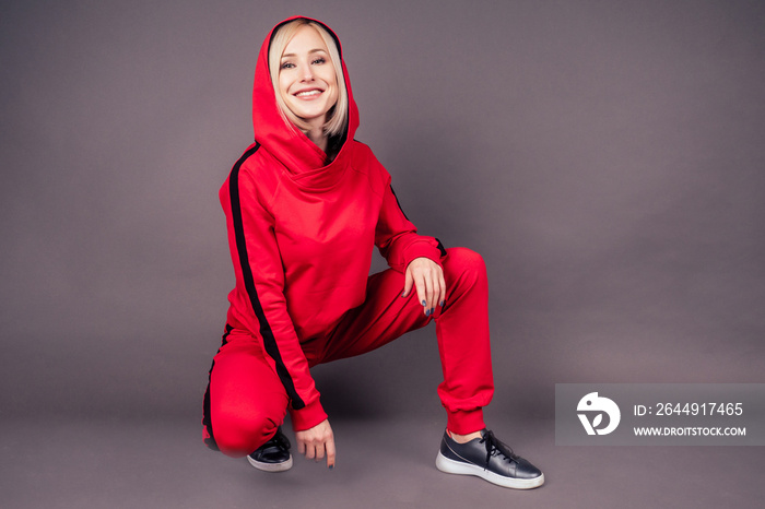 portrait of a beautiful blonde woman perfect skin and makeup put on hood hoodie sweatshirt red tracksuit sports suit hip hop dancer in studio on black background.Bob short hairstyle sensual style