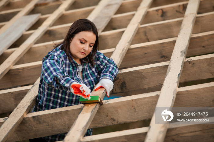 The young woman worker processes boards with stain