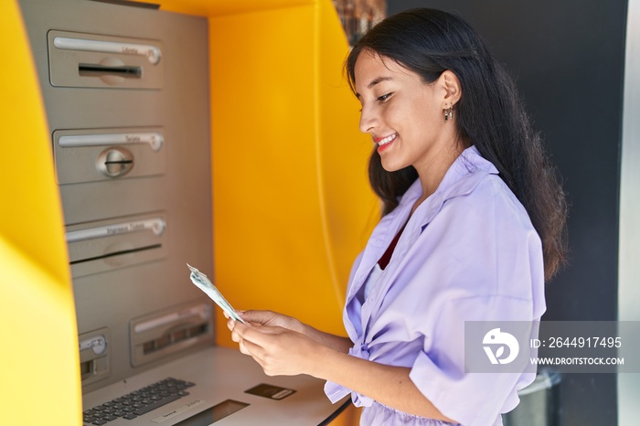 Young beautiful hispanic woman smiling confident holding dollars on bank teller at street