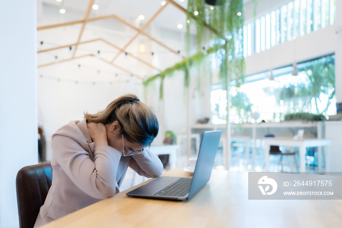 Office syndrome concept. Young asian businesswoman feeling pain in neck after working on computer laptop for a long time in a coffee shop cafe