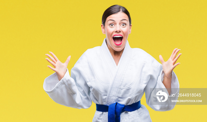 Young beautiful woman wearing karate kimono uniform over isolated background celebrating crazy and amazed for success with arms raised and open eyes screaming excited. Winner concept