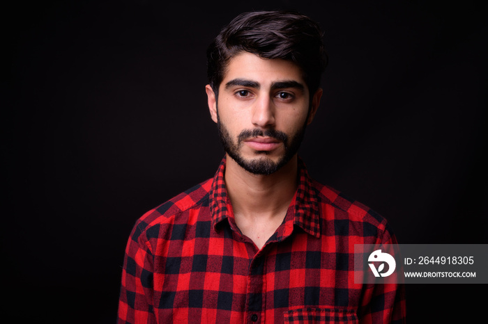 Young handsome bearded Persian man against black background