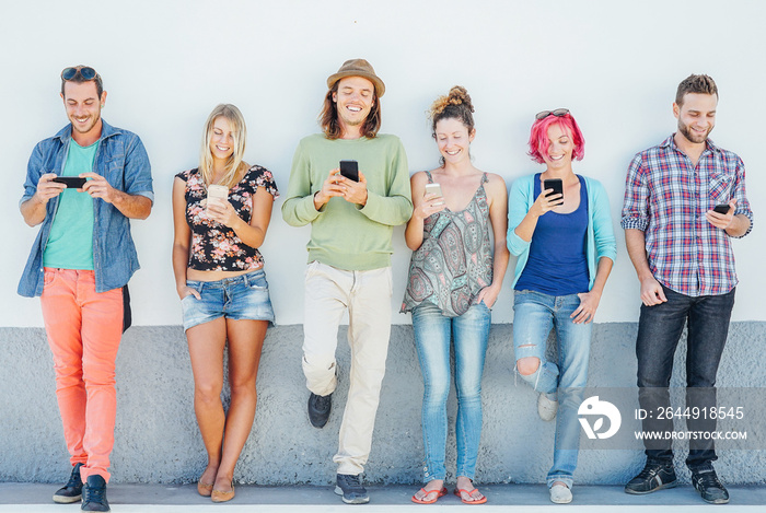 Young people watching on their smart mobile phones leaning on a wall - Generation addicted to new technology - Concept of youth addiction to social network trends