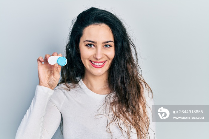 Young hispanic woman holding contact lenses looking positive and happy standing and smiling with a confident smile showing teeth