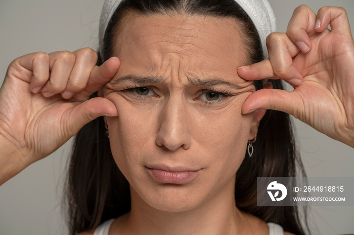 portrait of a young sad woman pinching her wrinkles next to her eyes