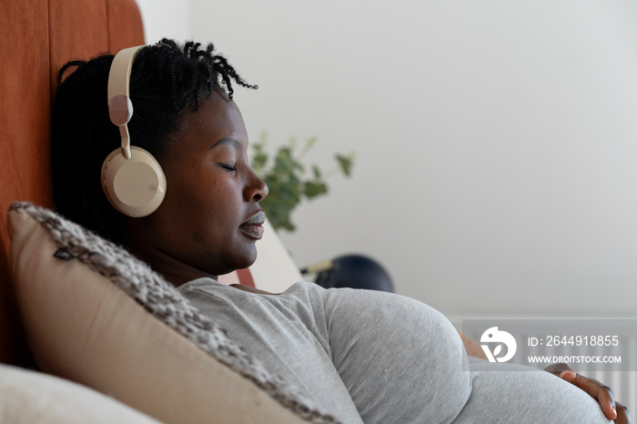 Pregnant woman with headphones relaxing on bed