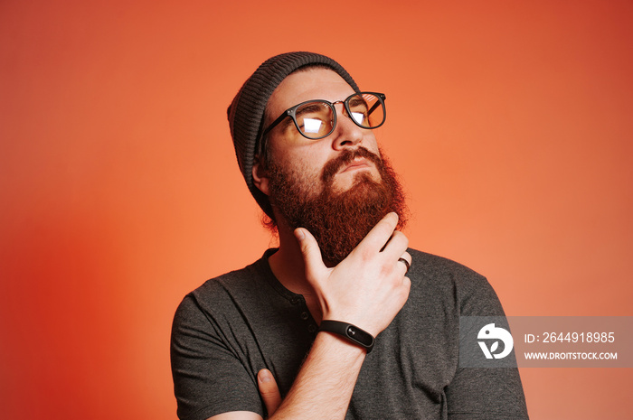 Bearded man with eyeglasses touching his beard and looking away, studio shot