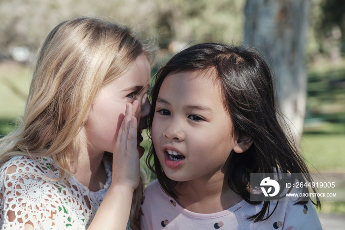 multiethnic young little girls playing kids Chinese whispering  in the park, best friends and positive friendship concept